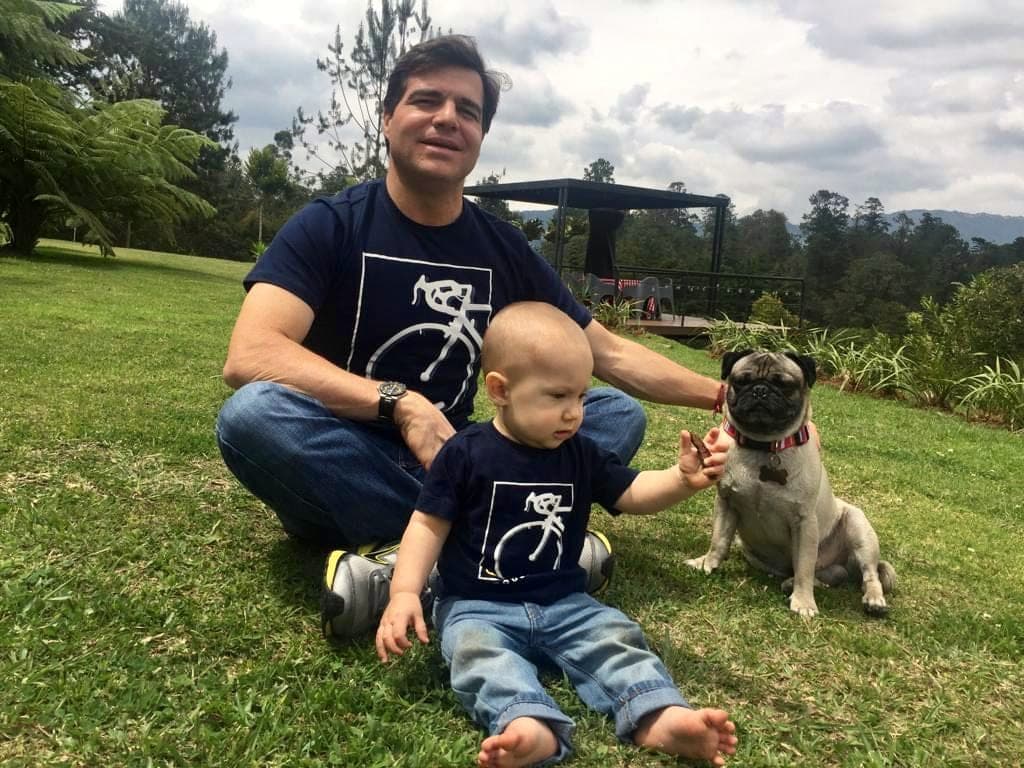 Alejandro Arbeláez A. sentado en el pasto con su hijo Pablo, bebé, y su perro Napoleón