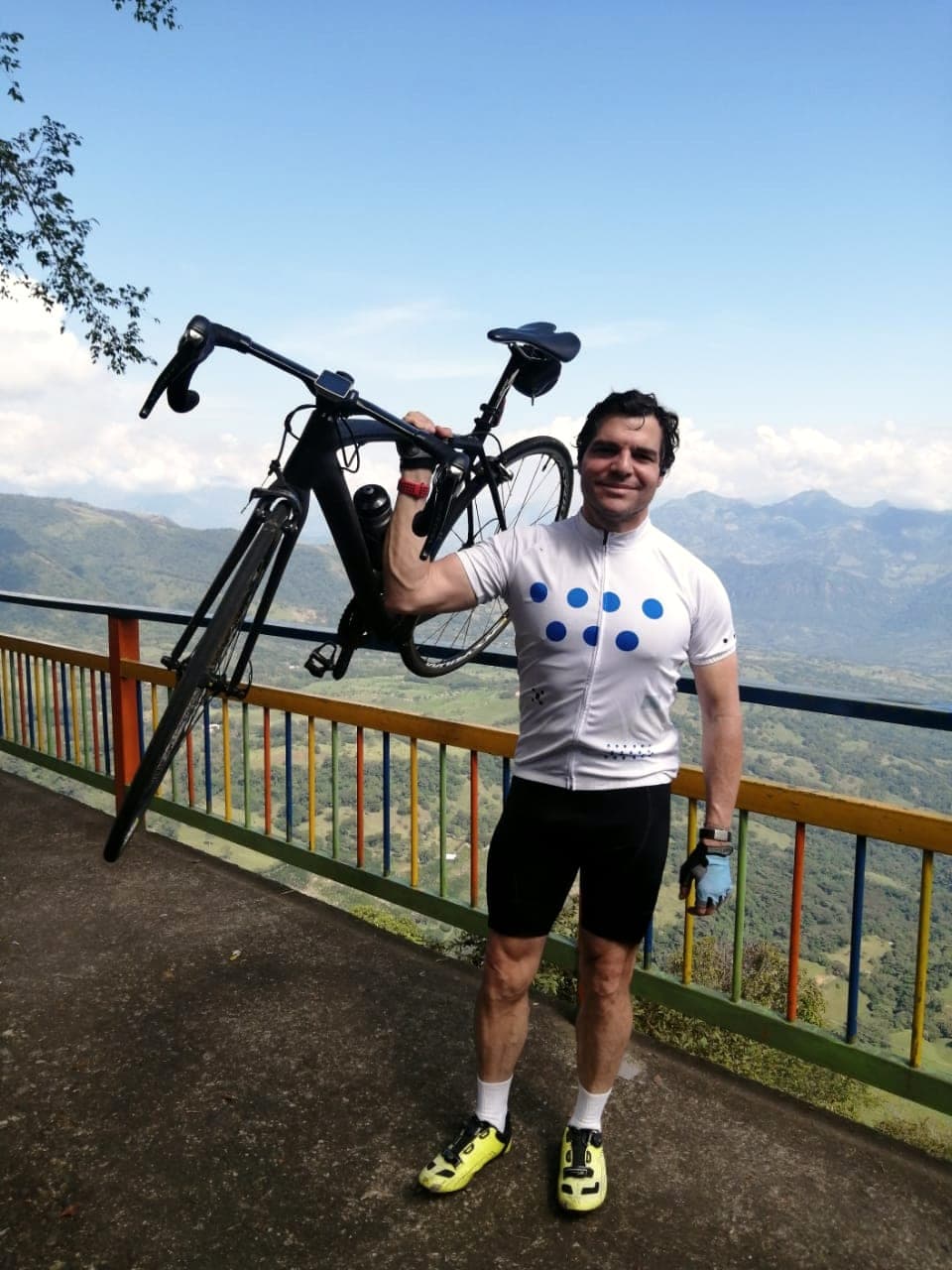Alejandro Arbeláez A. alza la bicicleta sobre la cabeza en un mirador, con las montañas al fondo