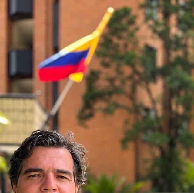 Retrato de Alejandro Arbeláez A. al aire libre, con la bandera de Colombia detrás