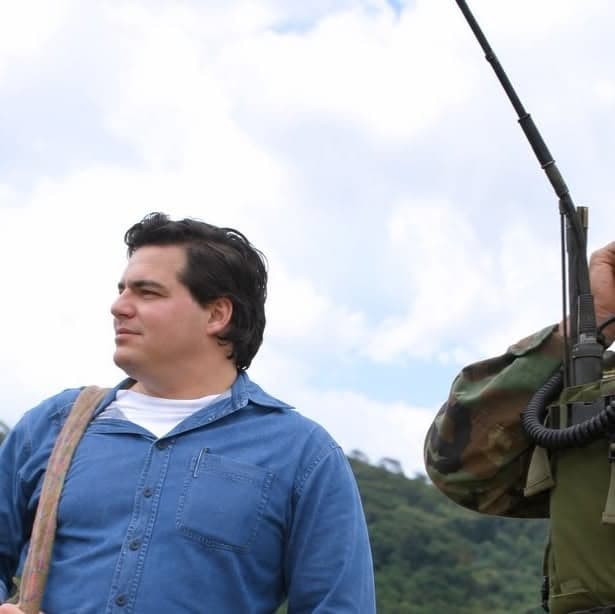 Alejandro Arbeláez A. de perfil, en camisa azul, en un campo de montaña junto a un soldado