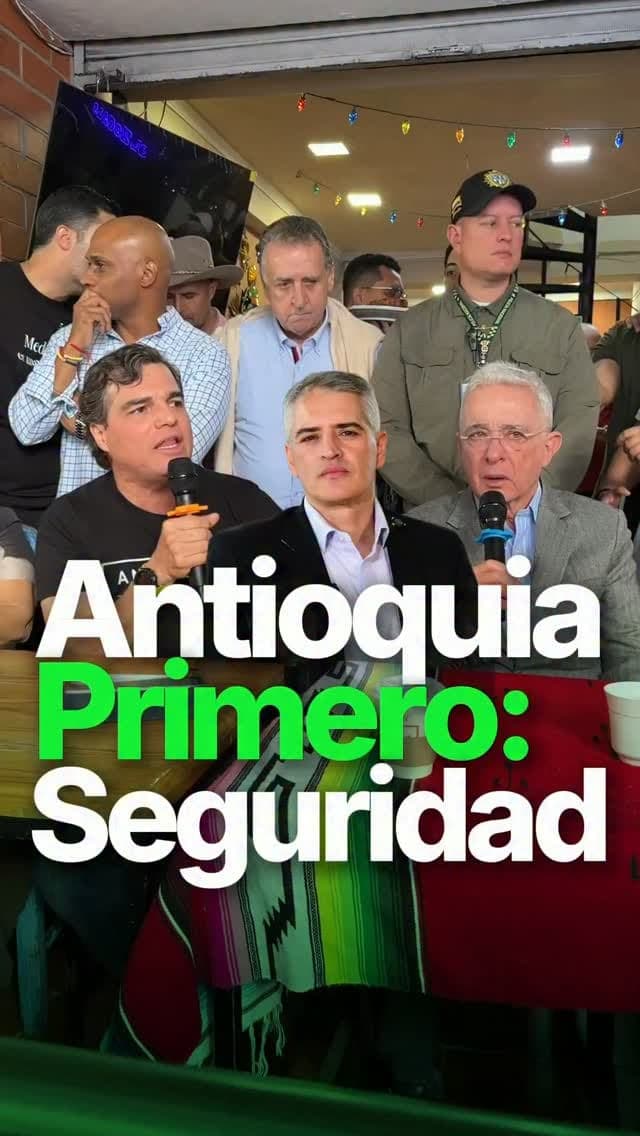 Alejandro Arbeláez A. habla con micrófono en un salón lleno, junto a Álvaro Uribe Vélez; texto «Antioquia Primero: Seguridad»