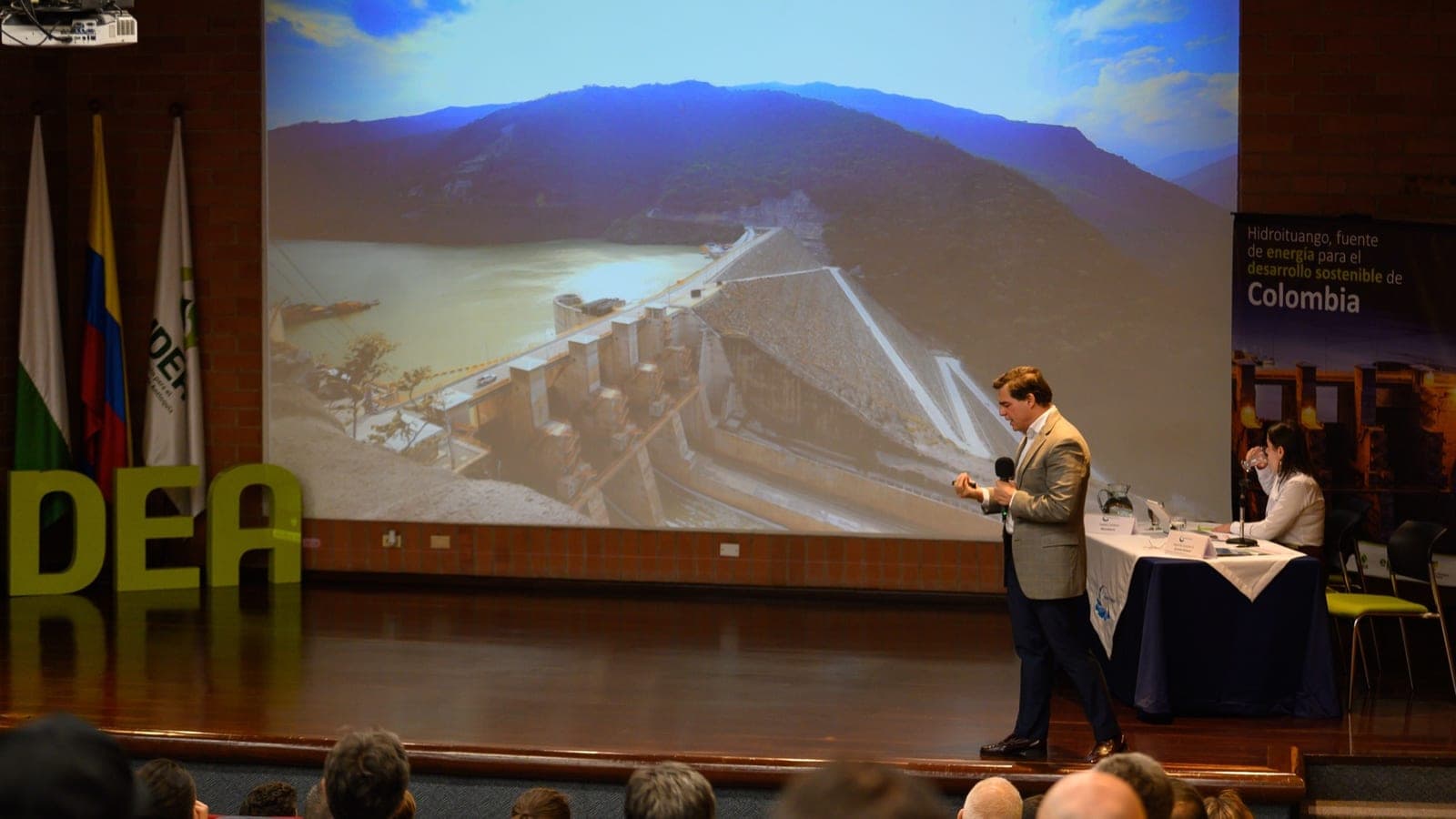 Alejandro Arbeláez A. expone ante un auditorio con la presa de Hidroituango proyectada detrás