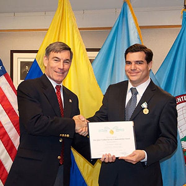 Alejandro Arbeláez A. recibe un reconocimiento del Centro de Estudios Hemisféricos de Defensa, frente a las banderas de Colombia y Estados Unidos